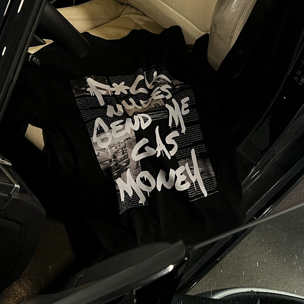 A black graphic t-shirt with bold white text reading 'F*CK NUDES SEND ME GAS MONEY' is displayed on white leather car seat. 